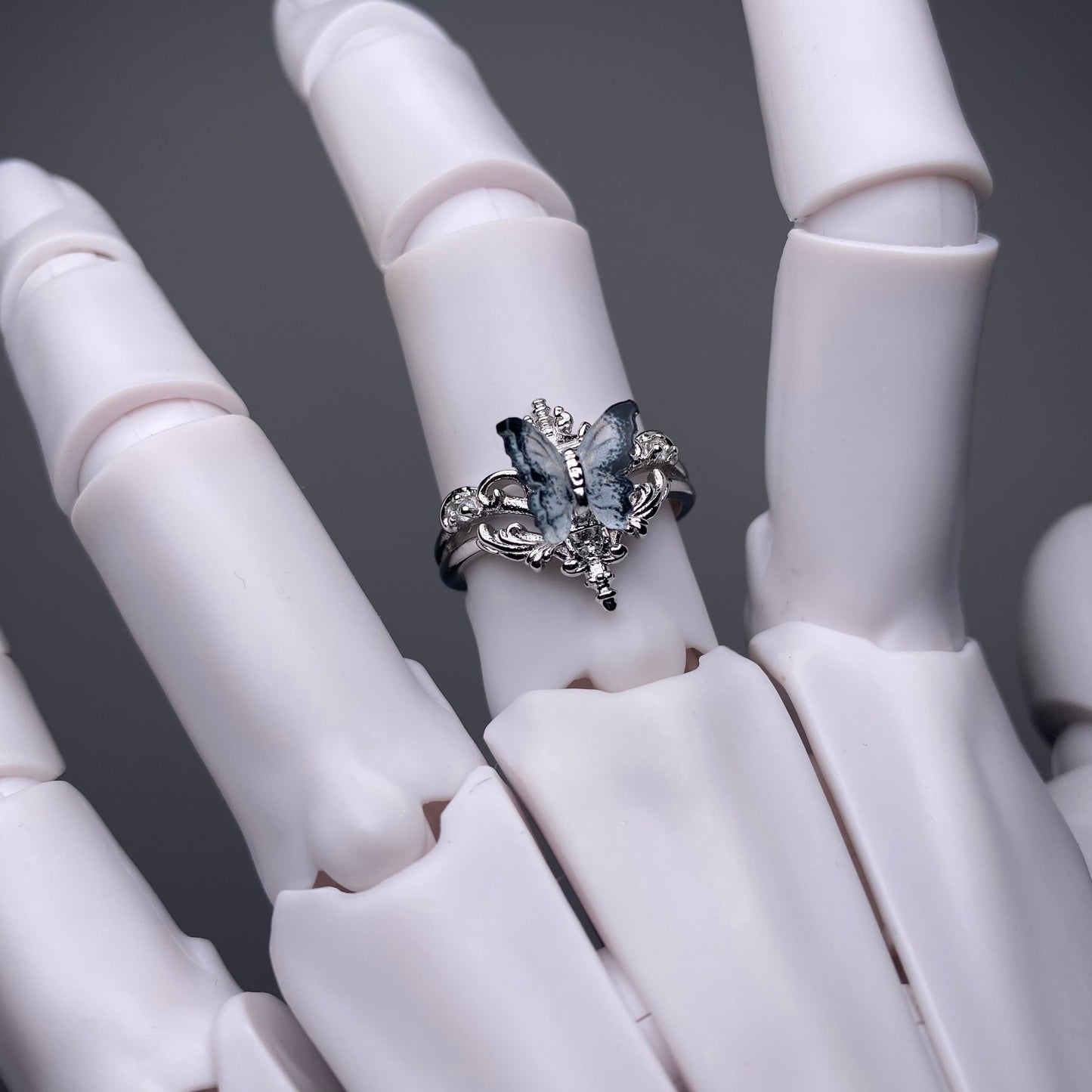 Silver ring with blue gemstones on a white mannequin hand against a dark background