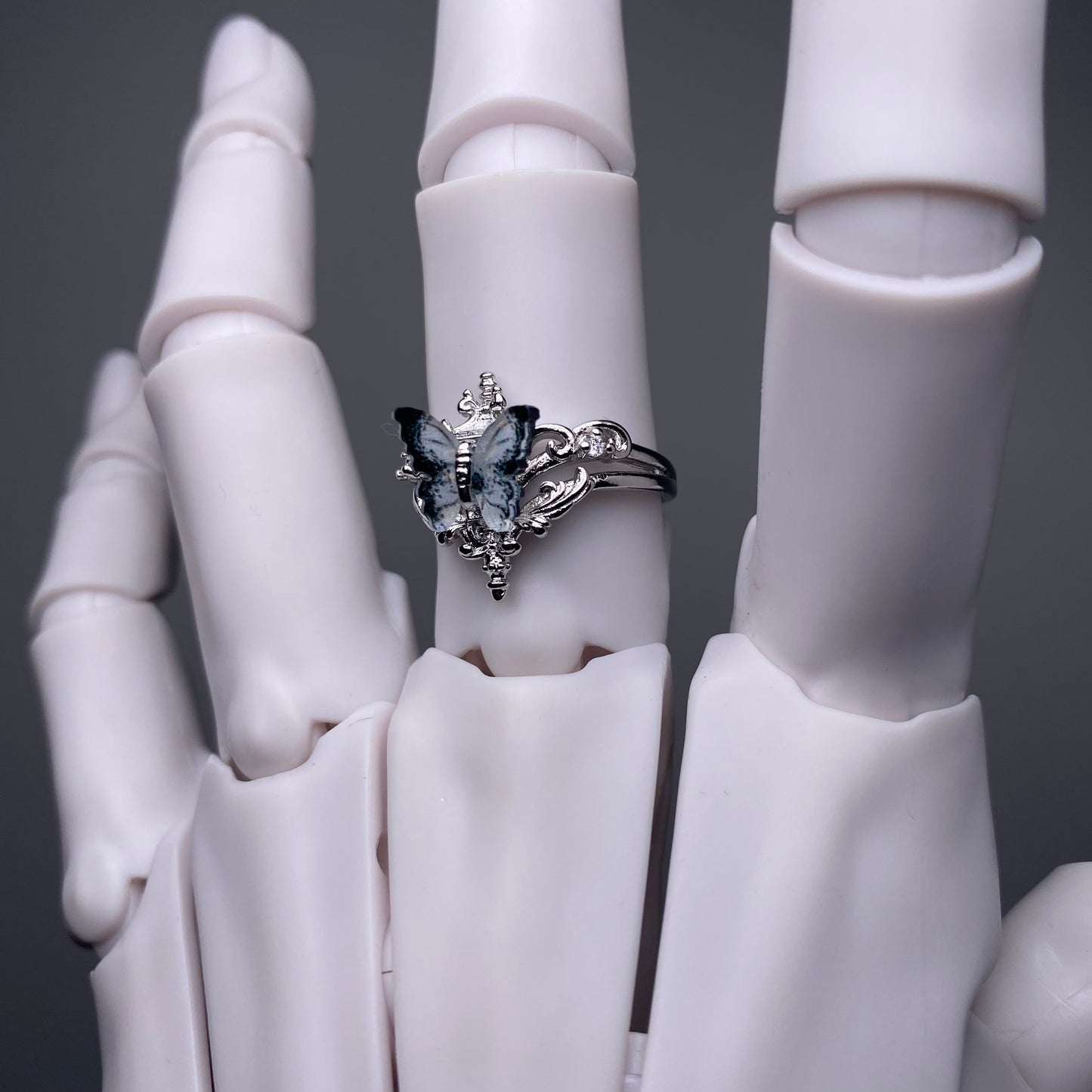 Silver ring with butterfly design on a white mannequin hand against a dark background