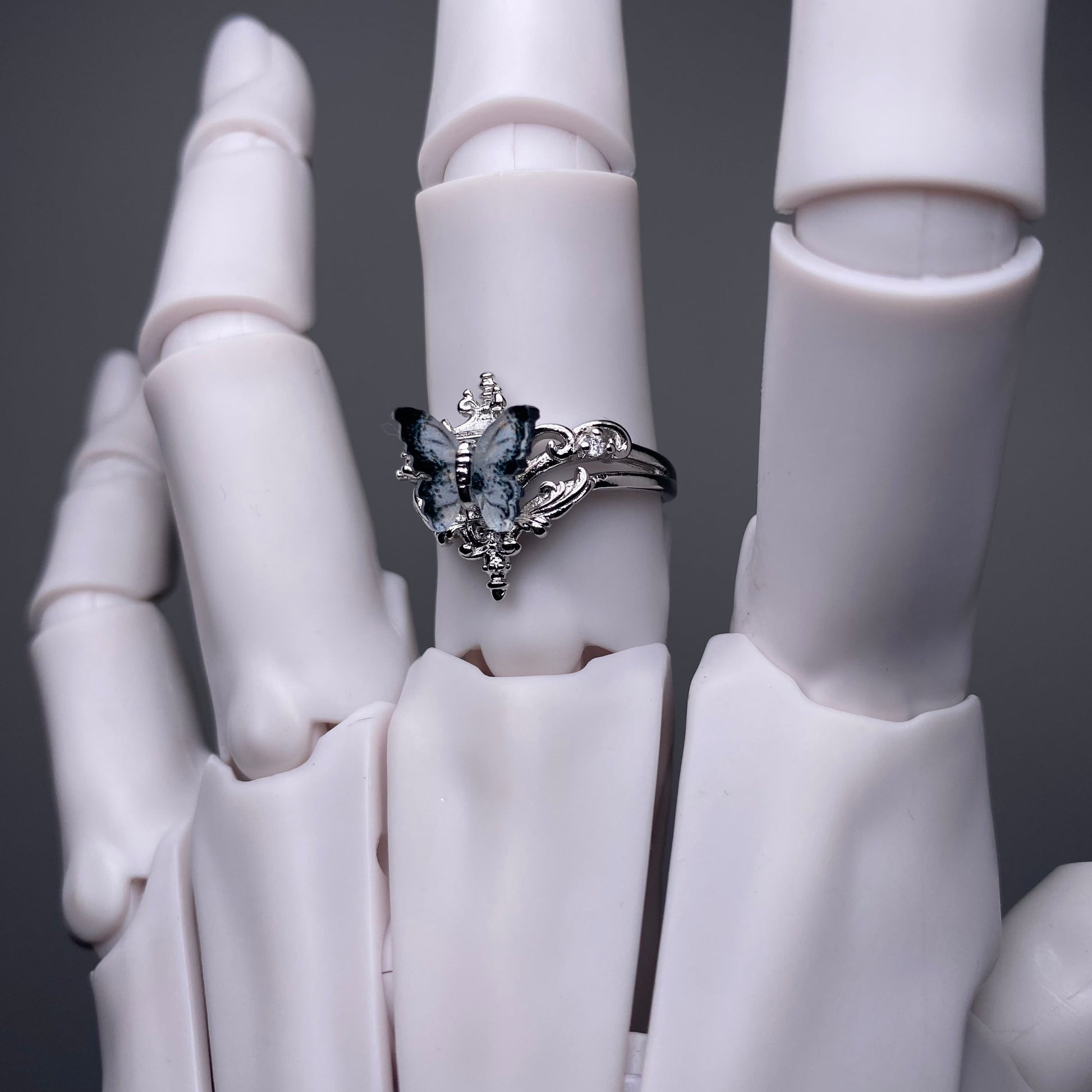 Silver ring with butterfly design on a white mannequin hand against a dark background